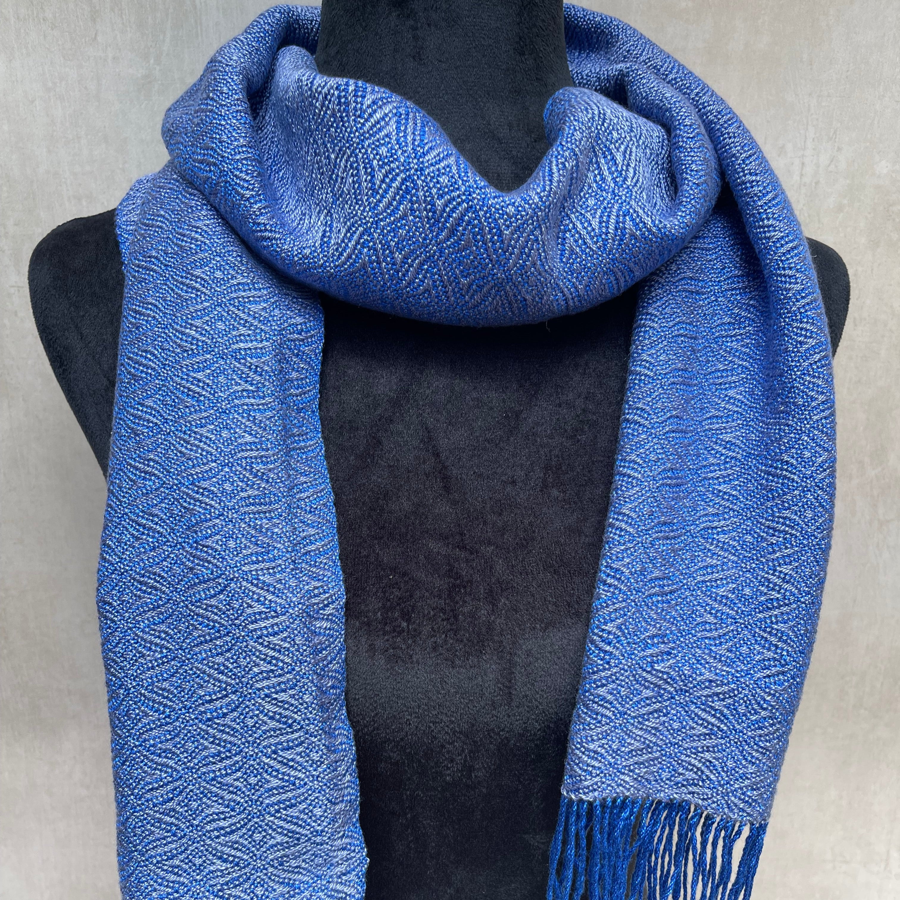 Blue patterned scarf with tassels draped over a black garment on a light gray background