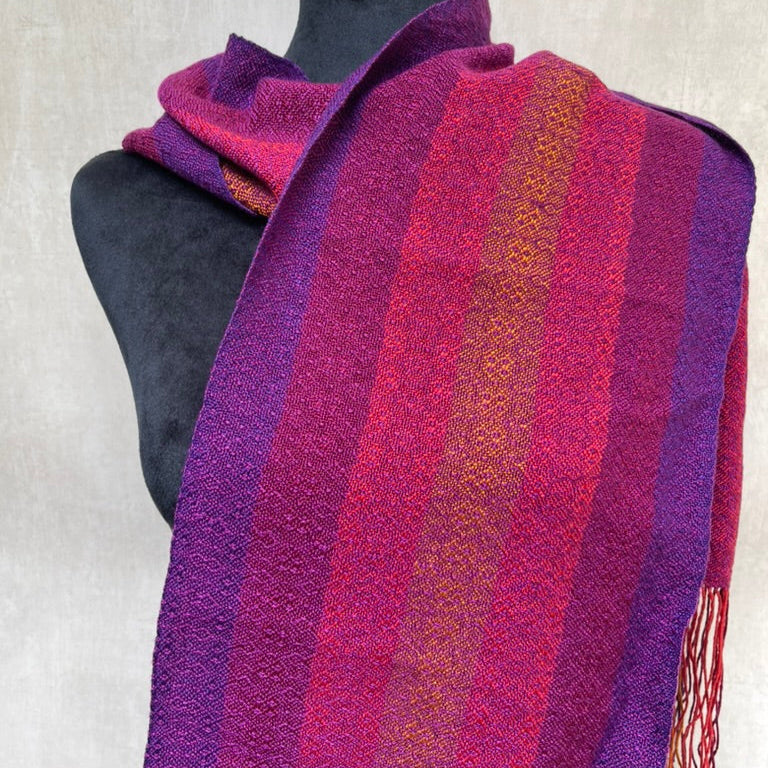 Striped scarf in purple and red on a mannequin against a neutral background
